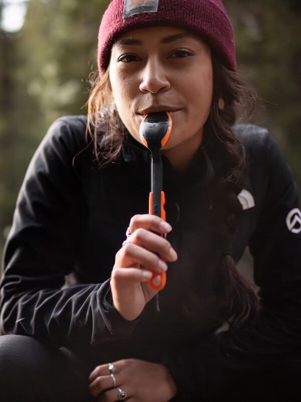 Woman outdoors with a beanie on and a spoon in her mouth