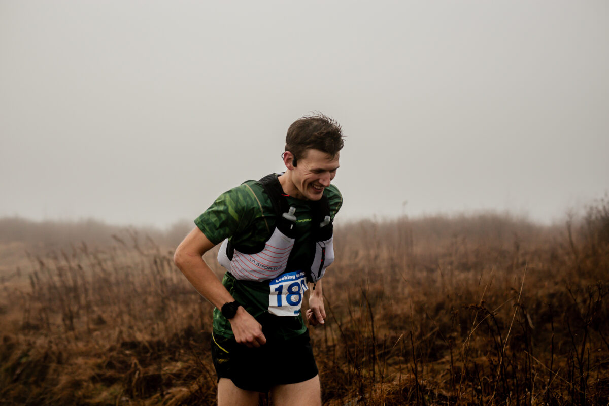 Man smiling as he runs a trail race in foggy weather